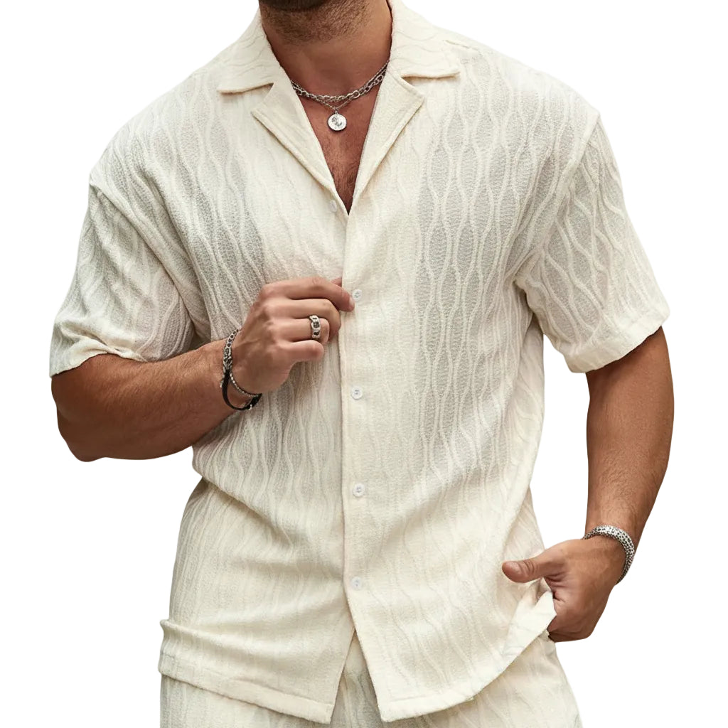 Man wearing a light-colored shirt and pants against a stone wall.