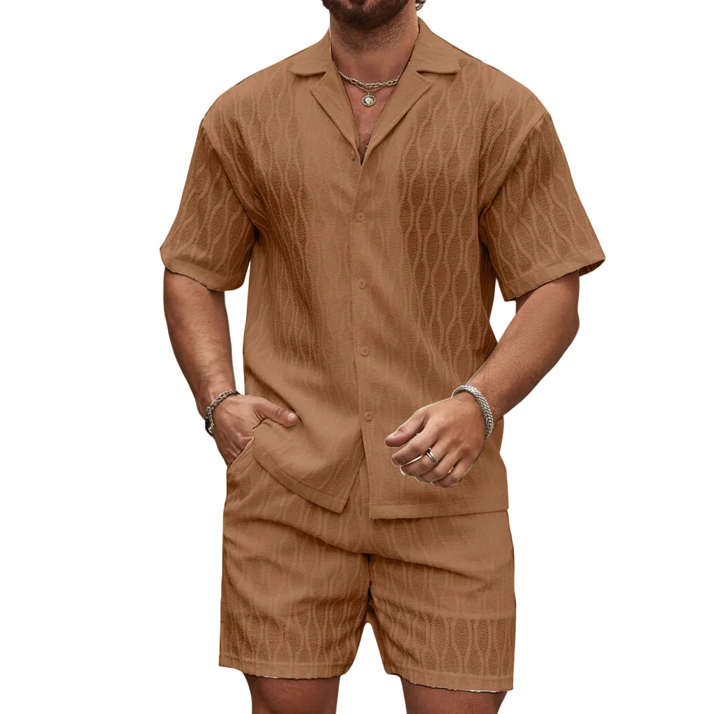 Man wearing a brown patterned shirt and shorts set against a stone wall.