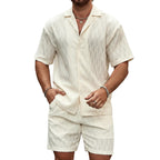 Man wearing a white textured shirt and shorts set against a stone wall.